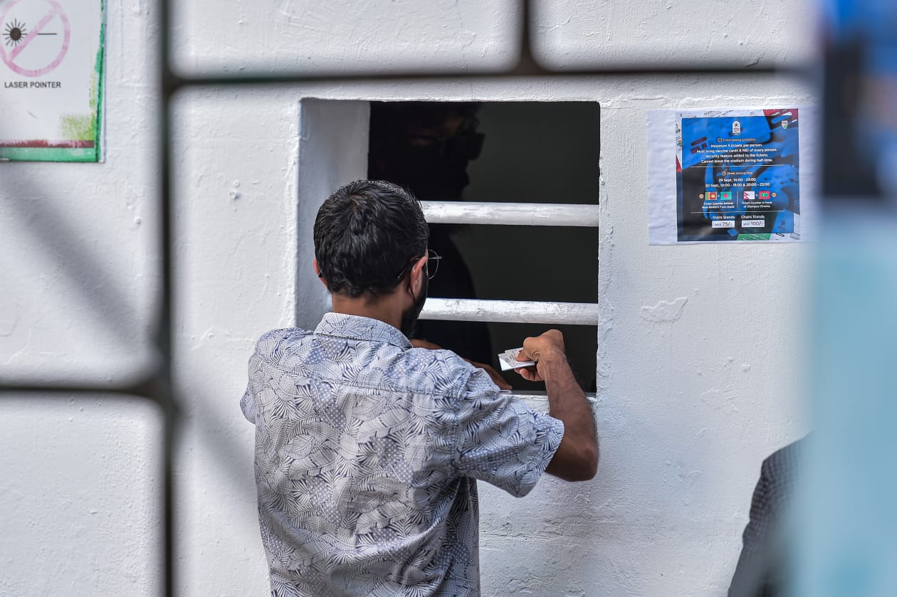 މާލެ: އަންނަ ހުކުރު ދުވަހު މާލޭގައި ފެށުމަށް ހަމަޖެހިފައިވާ އުރީދޫ ސާފް ޗެމްޕިއަންޝިޕްގެ ޓިކެޓު ވިއްކަން މިއަދު މެންދުރު ފަހު ފެށިއިރު ގިނަ ބަޔަކު ވަނީ ޓިކެޓް ގަންނަން ކިއޫ ހަދާފައި: މި ފަހަރުގެ ސާފް ޗެމްޕިއަންޝިޕްގައި ޓިކެޓް ވިއްކާނީ އަބަދުވެސް ކުރިއަށް އޮންނަ "މެޗު ޑޭ" އަކަށް: ކޮންމެ މީހަކަށް ގިނަވެގެން ފަސް ޓިކެޓް ލިބޭއިރު، އެ ޓިކެޓްތަކަށް ދަނޑަށް ވަންނަ މީހުންގެ އައިޑީ ކާޑާއި ވެކްސިން ކާޑު ބޭނުންވާނެ-- ފޮޓޯ: ހުސެއިން ޝަޔާހު/ އަދަދު 