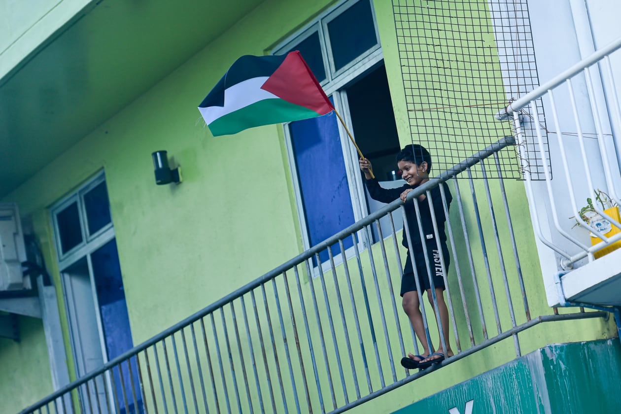 ދިވެހިން ފަލަސްތީނު ރައްޔިތުންނަށް އޮތް ލޯބި ދައްކާލުމުގެ ގޮތުން މިއަދު ބޭއްވި ހަރަކާތް ކުރިއަށްދިޔަ ވަގުތު, ގެއެއްގެ ބެލްކަނީގައި ކުޑަކުއްޖަކު ފަލަސްތީނު ދިދައެއް ހޫރަނީ---ފޮޓޯ: ހުސައިން ވަހީދު / އަދަދު
