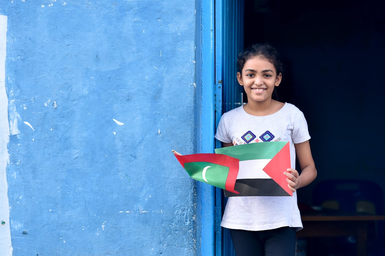 ދިވެހިން ފަލަސްތީނު ރައްޔިތުންނަށް އޮތް ލޯބި ދައްކާލުމުގެ ގޮތުން މިއަދު ބޭއްވި ހަރަކާތް ކުރިއަށްދިޔަ ވަގުތު, ގެއެއްގެ ދޮރުމަތީ ކުޑަކުއްޖަކު ފަލަސްތީނާއި ރާއްޖޭގެ ދިދައެއް ހިފައިގެން---ފޮޓޯ: ހުސައިން ޝަޔާހު / އަދަދު